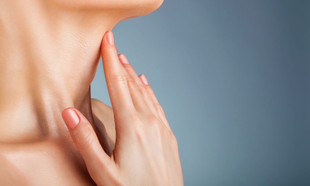 Closeup of a young woman regards her neck on a gray background